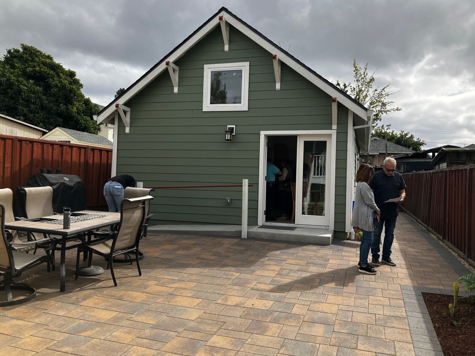 Two people stand in the yard in front of a green cottage.